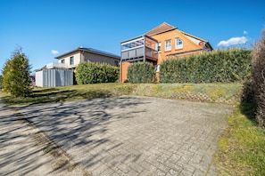 Een woonwijk met een verharde oprit, een huis met balkon en een haag.