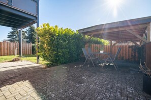 Een terras met een houten pergola, een tafel en stoelen, en een vloer van baksteen.