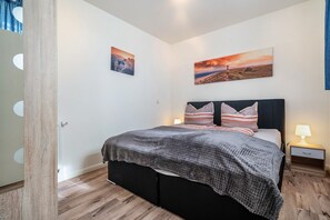 Een slaapkamer met een bed, twee kussens, een nachtkastje en twee aan de muur hangende foto's.