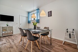 Een moderne eetruimte met een tafel, stoelen en een aan de muur bevestigde televisie.