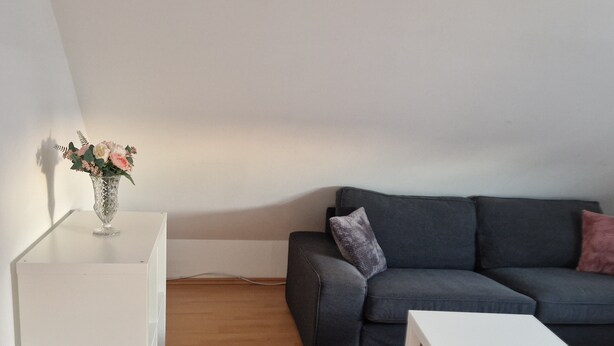 A modern living room with a grey sofa, a white coffee table, and a white side table with a vase of flowers. - Fantastic Apartment in the Heart of Wedel (Wedel)