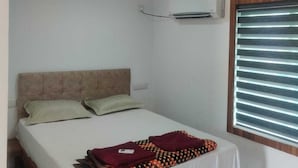 Une chambre à coucher avec un lit, des oreillers, une couverture, un appareil de climatisation et une fenêtre avec des stores.