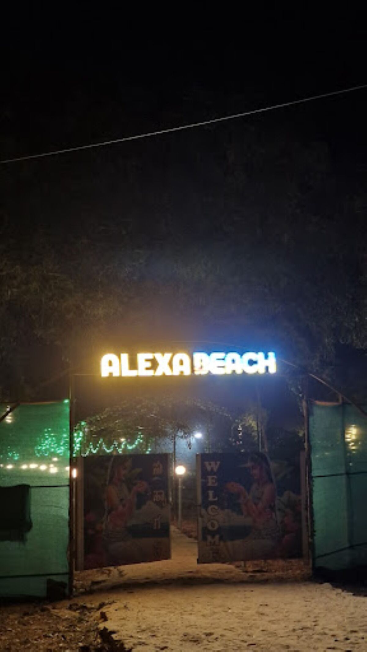 A neon sign reading "ALEXA BEACH" above a doorway with a "WELCOME" sign.