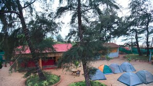 Un terrain de camping avec des tentes, des arbres et un bâtiment doté d’un toit rouge.