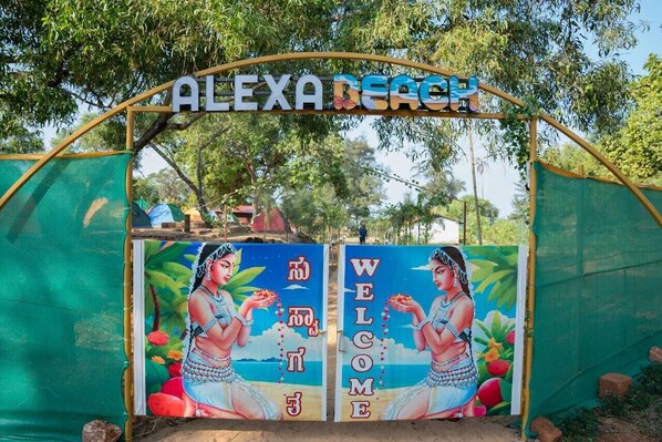 Adgang til stranden med et skilt, der viser "ALEXA BEACH", og et mural af to personer, der holder frugt.