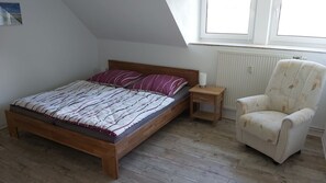 Un dormitorio con cama de madera, mesita de noche, silla y ventana con vistas.