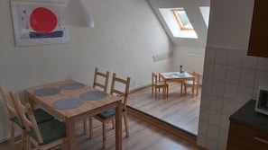 Ein Zimmer mit Esstisch, Stühlen, einer kleinen Küchenzeile und einem Oberlicht.