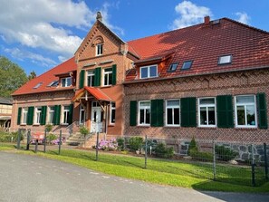 Un edificio in mattoni di due piani con persiane verdi, tetto rosso e un piccolo portico anteriore.