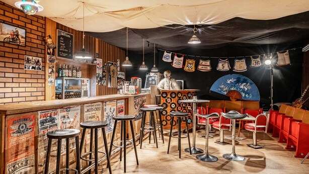 A bar area with stools, a counter, and a wall with posters and memorabilia.