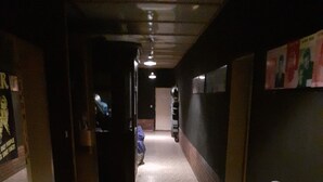 A hallway with a tiled floor, a row of brown chairs on the right, and a poster on the left wall.