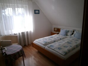 Une chambre à coucher avec un lit, une chaise, une petite table et une fenêtre avec des rideaux.