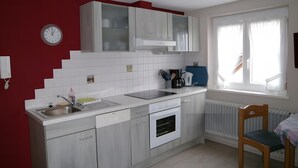 Une cuisine avec des meubles blancs, un évier, un four et une fenêtre avec des rideaux.