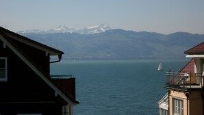 Un bâtiment doté d’un balcon donnant sur un lac paisible et sur des montagnes lointaines aux sommets enneigés.