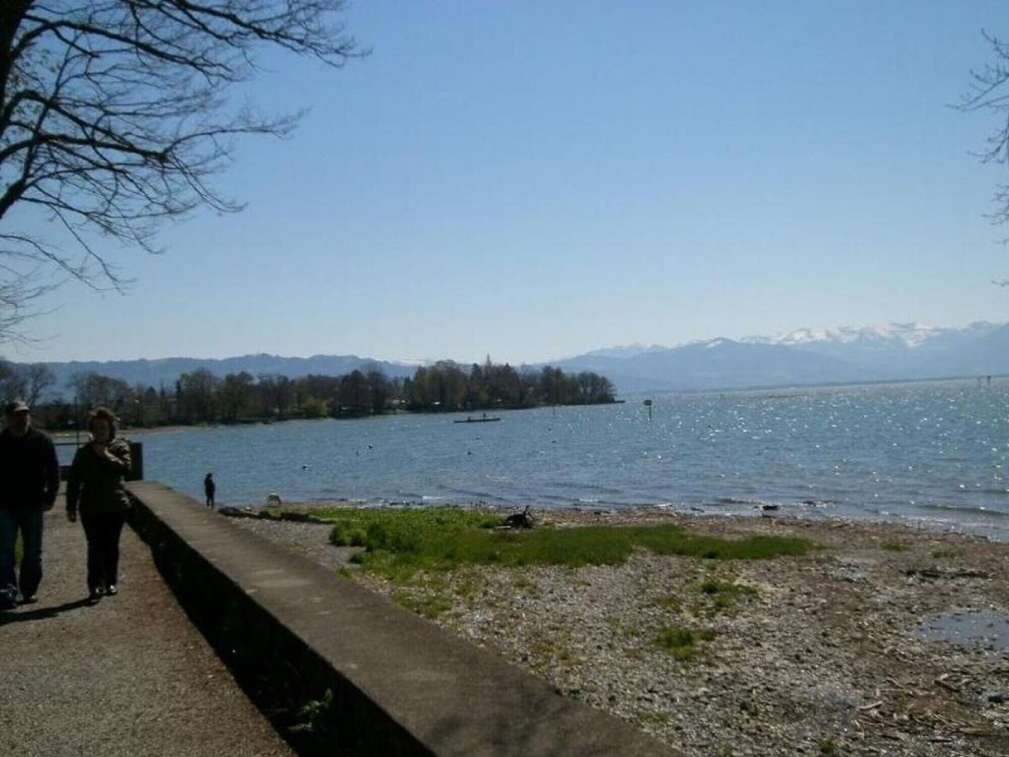 Une vue sur le lac, avec une promenade en béton, des eaux calmes et des montagnes à l’horizon.