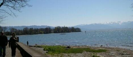 Une vue sur le lac, avec une promenade en béton, des eaux calmes et des montagnes à l’horizon.