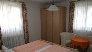 Une chambre d’hôtel avec un lit, une chaise, une petite table ronde et une armoire.