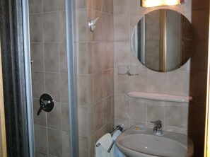 Un baño con lavamanos, espejo, toallero y puerta de ducha.