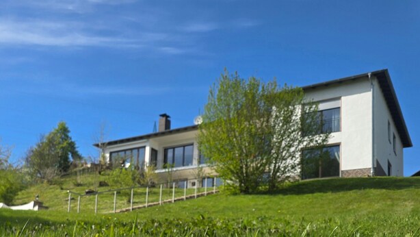 Une maison moderne avec un toit en pente, de grandes fenêtres et une pelouse bien entretenue.