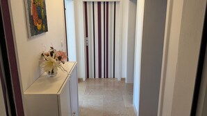 Un couloir avec une porte à rayures, un tableau accroché au mur et un vase rempli de fleurs posé sur une commode.