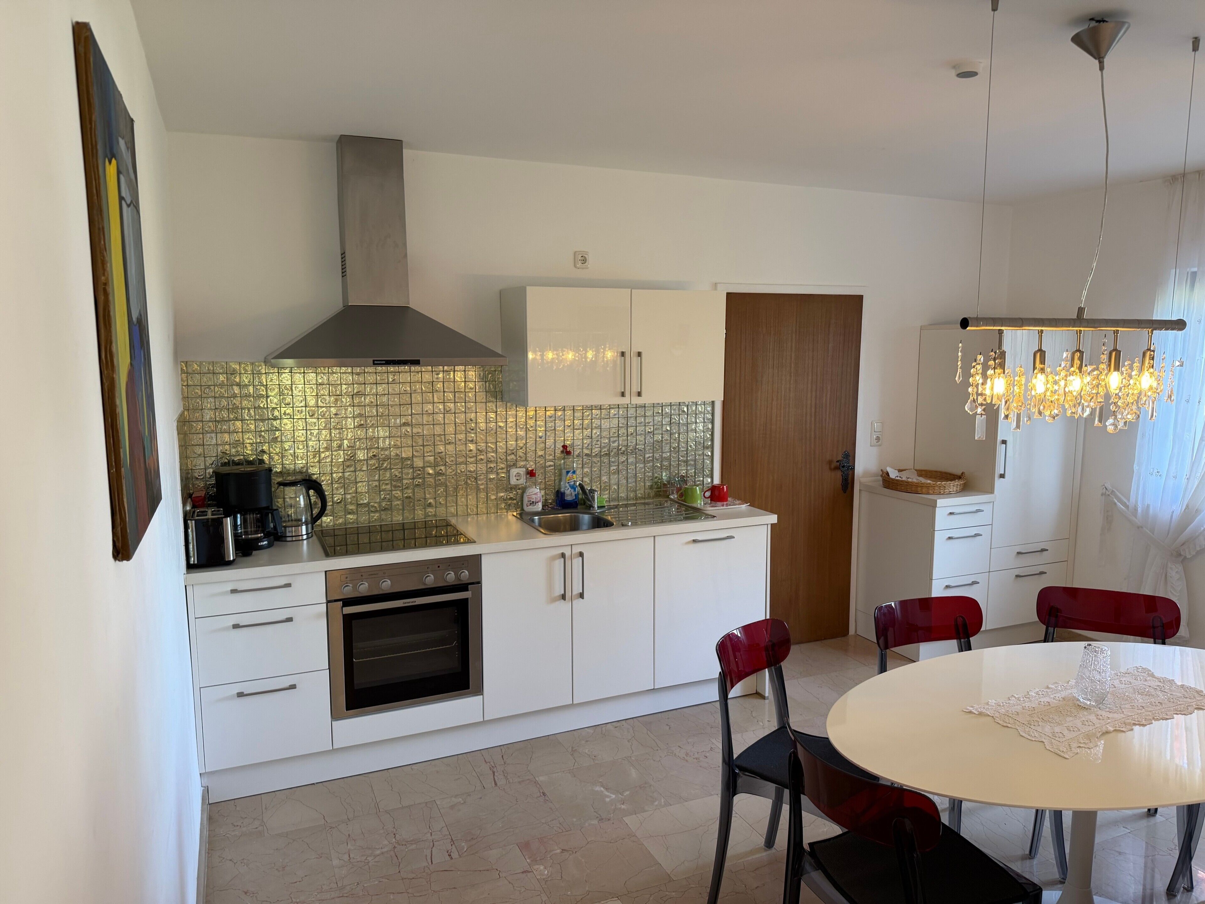Une cuisine moderne équipée d’un four encastré, d’une cuisinière à gaz et d’une hotte en acier inoxydable. On y trouve également un coin repas avec une table ronde et des chaises rouges.