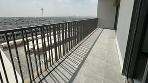 Un balcon doté d’une rambarde en métal, donnant sur un parking et sur des bâtiments situés au loin.