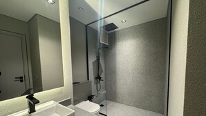 Une salle de bain moderne avec un lavabo blanc, des toilettes et une douche séparée par une paroi de verre.