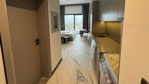 Une chambre d’hôtel comprenant un lit, un petit coin salon, une kitchenette et une grande fenêtre donnant sur la ville.
