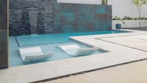 Een modern buitenzwembadgedeelte met een stenen muur, een waterval en twee ligstoelen.