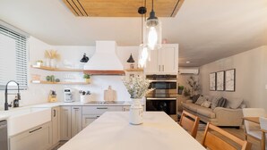 Een moderne keuken met witte kasten, een centraal eiland en een eethoek met houten stoelen.