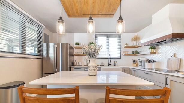 Een moderne keuken met een centraal eiland, roestvrijstalen apparatuur, hanglampen en houten keukenkastjes.