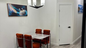 Ein moderner Essbereich mit einem weißen Tisch und orangefarbenen Stühlen, einem Schwane-Gemälde an der Wand und einer weißen Tür im Hintergrund.