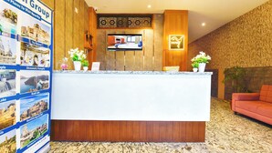 Een hotel receptie met een houten receptiebalie, een flatscreen televisie en een muur met een poster van lokale bezienswaardigheden.