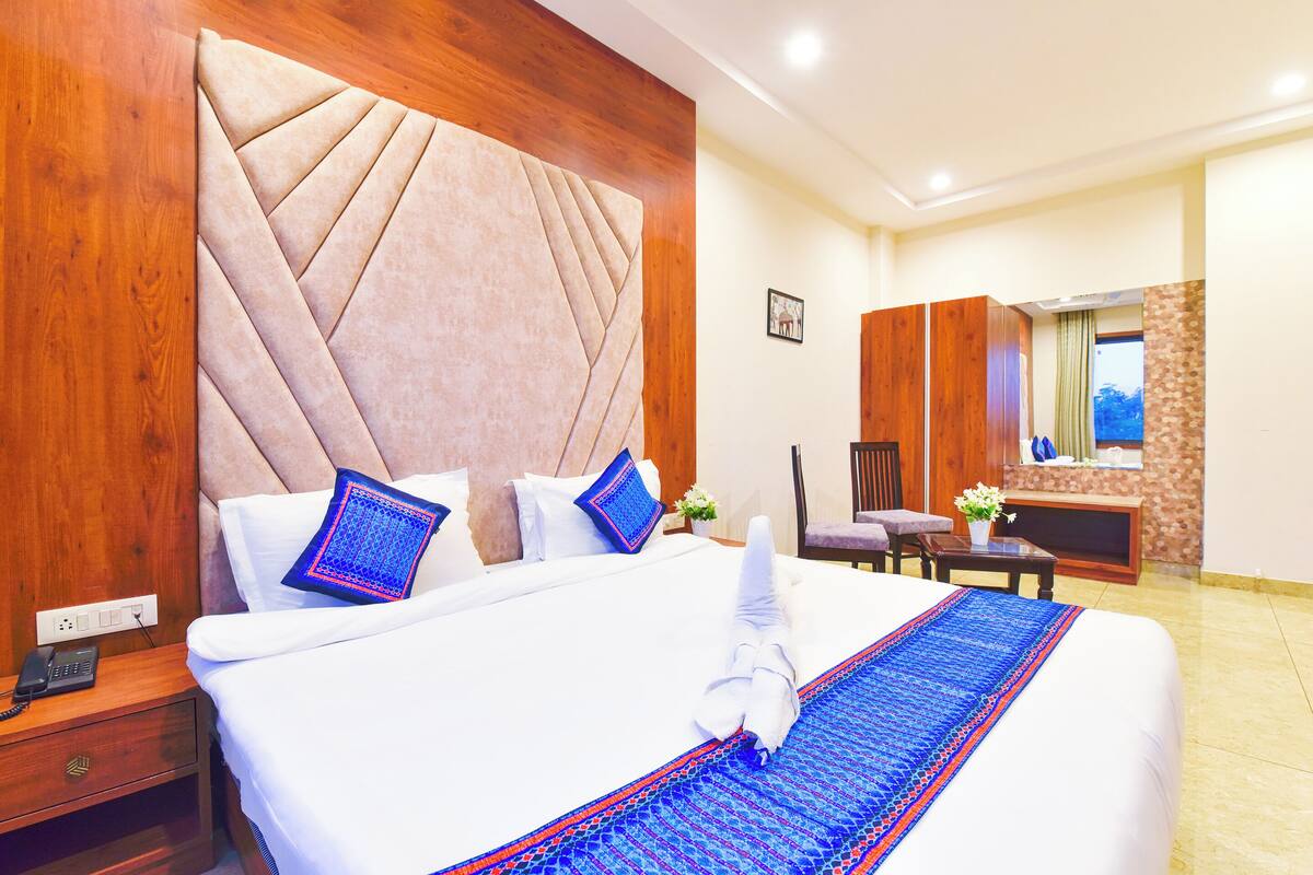A hotel room with a large bed, wooden headboard, and a small desk with a chair.