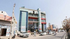 Un edificio de varios pisos con letreros comerciales, una gran estructura cilíndrica y automóviles estacionados en la calle.