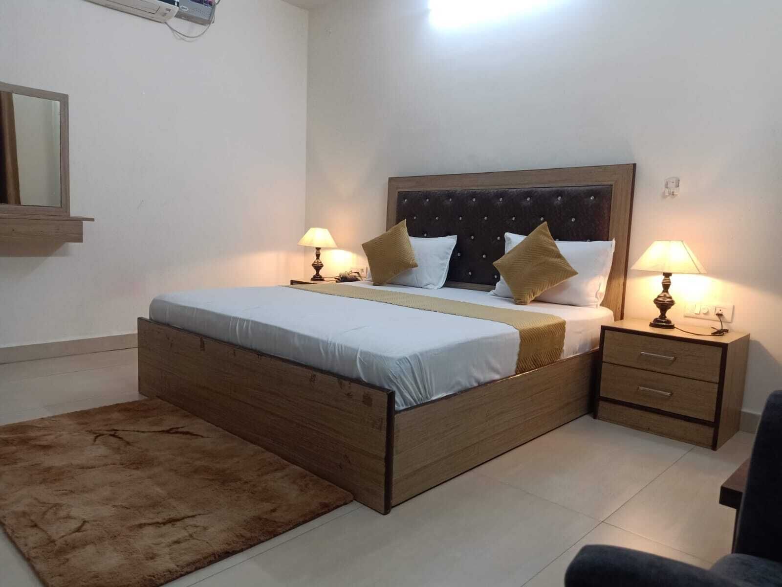 A bedroom with a wooden bed, two bedside tables with lamps, a small rug, and a mirror on the wall.