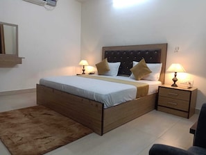 A bedroom with a wooden bed, two bedside tables with lamps, a small rug, and a mirror on the wall.