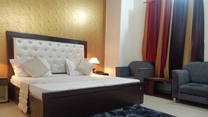 Un dormitorio con una cama grande, un cabecero oscuro, un tapete azul, una silla y una mesita de noche con una lámpara.
