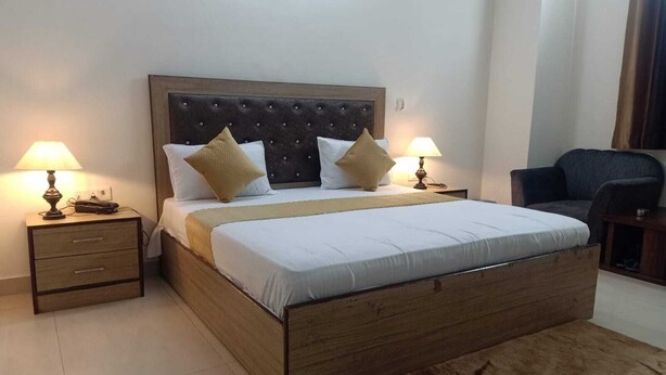 Un dormitorio ordenado con un cabecero de madera, dos mesitas de noche con lámparas y una silla.