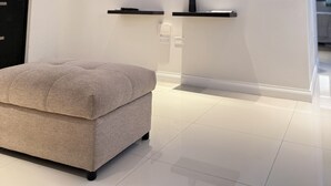 A modern living room with a flat-screen TV mounted on the wall, a grey ottoman, and a ceiling with blue LED lighting.