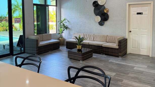 A modern living room with a sofa, coffee table, and chairs. There is a pool visible through the glass doors.
