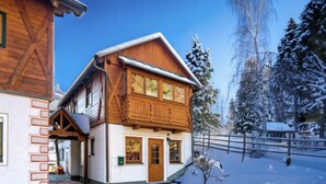 Una casa a due piani in legno con un balcone, un garage e un paesaggio innevato.