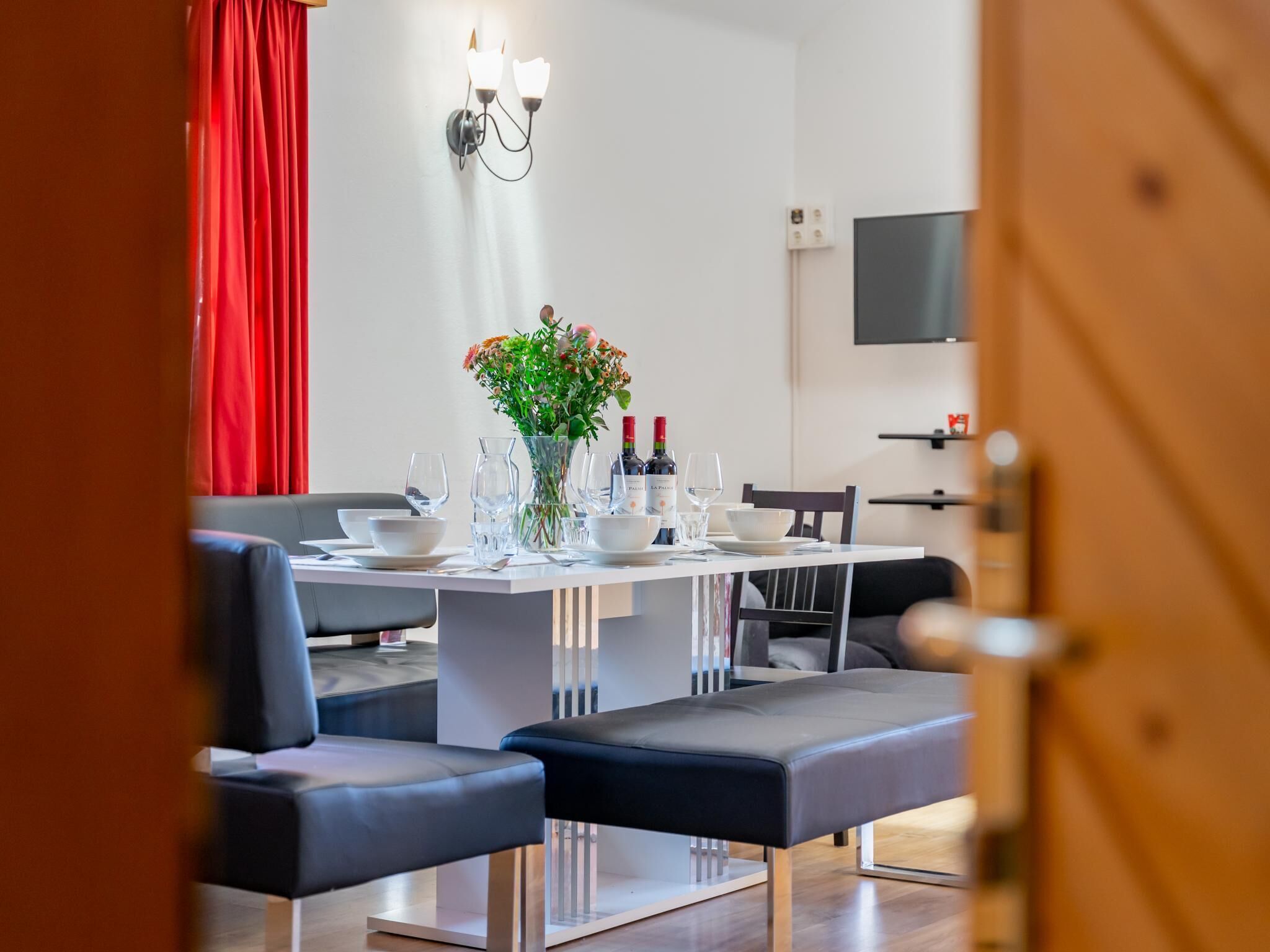 Een moderne eetruimte met een witte tafel gedekt voor vier personen, omringd door grijs gestoffeerde stoelen. Op tafel staan een vaas met bloemen en flessen wijn.