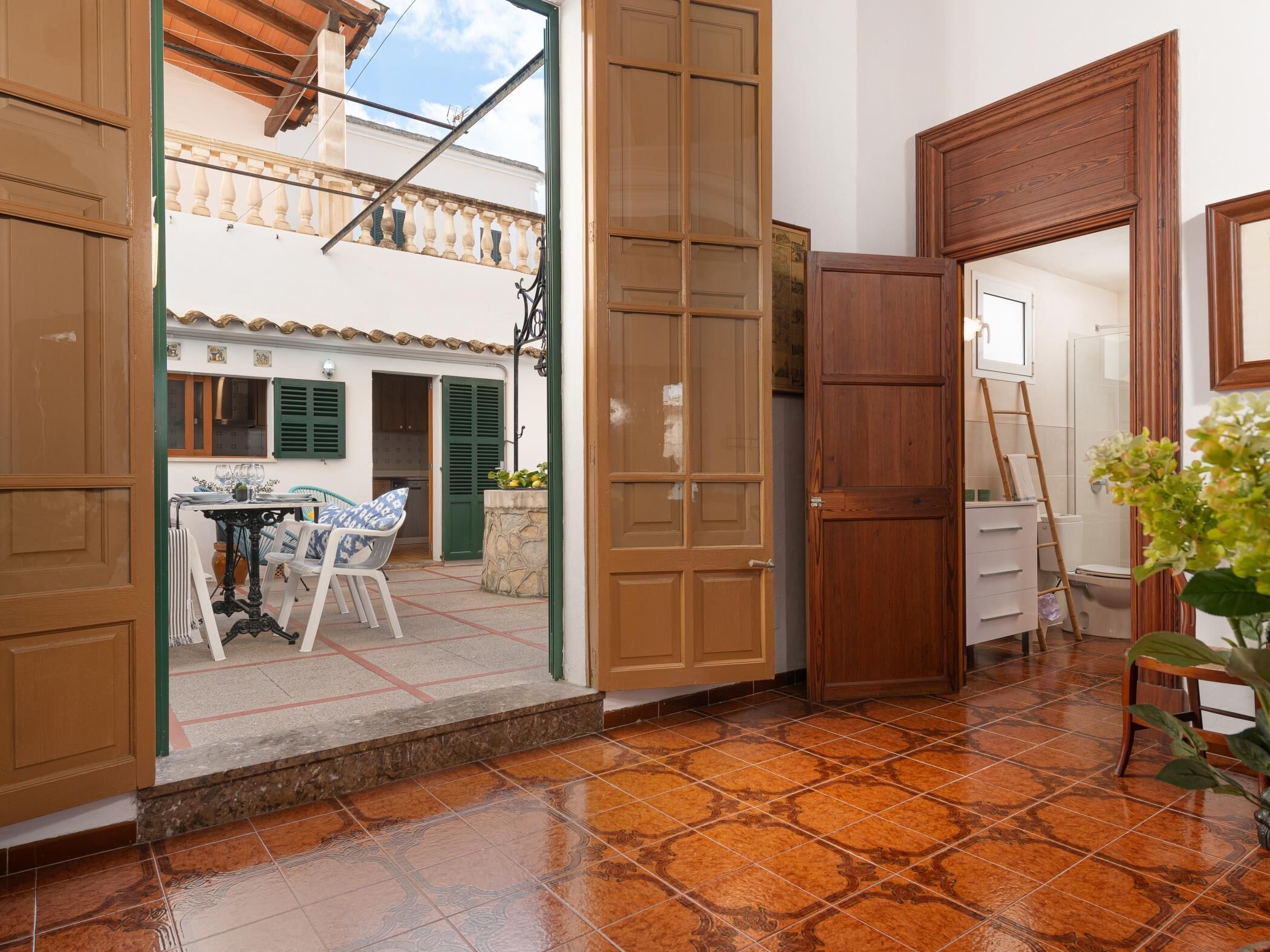 A room with a tiled floor, wooden doors, a table with chairs, and a view of the outside balcony.