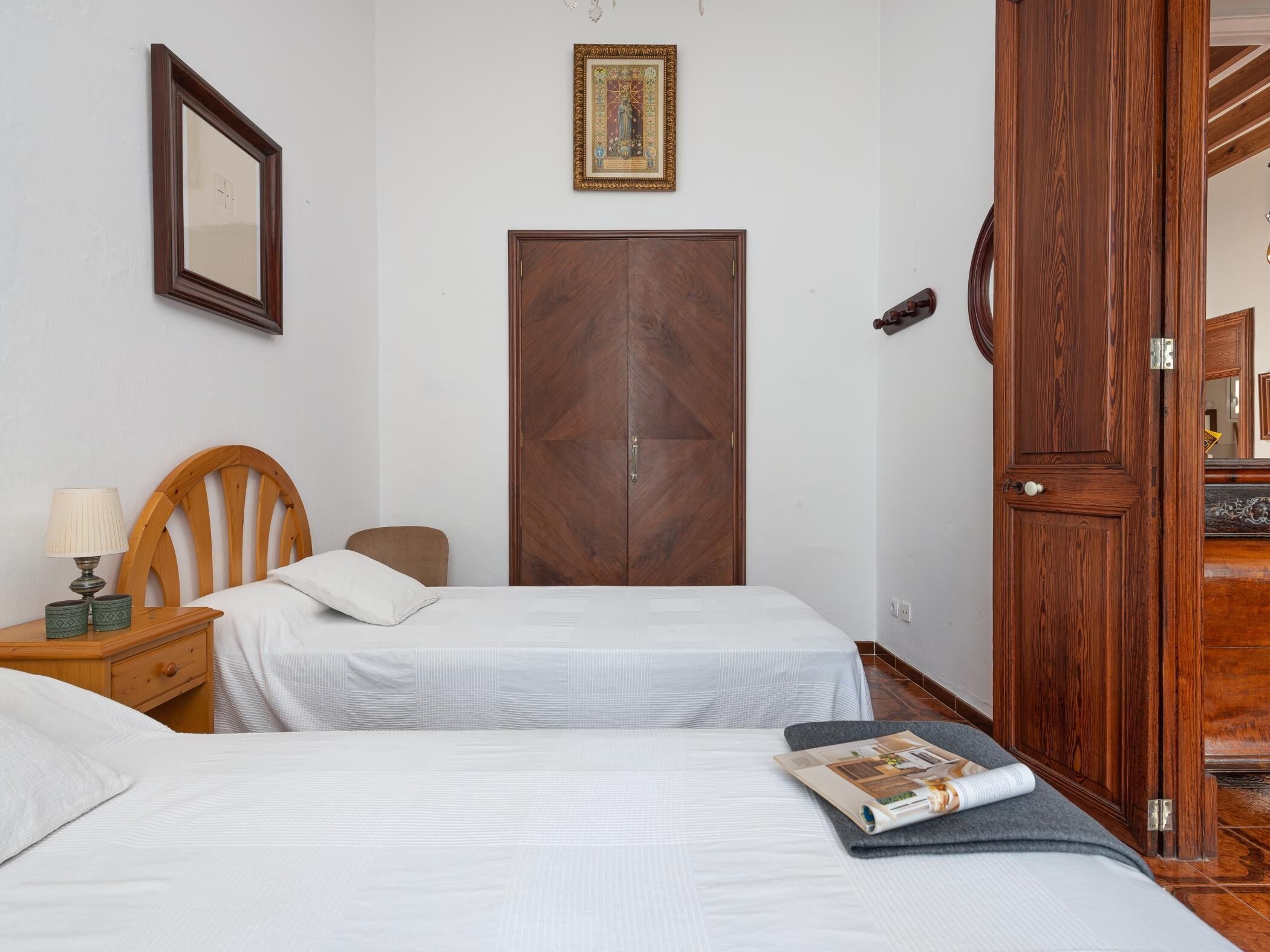 Een slaapkamer met twee bedden, een houten garderobe, een ingelijst schilderij aan de muur en een deur met een spiegel.