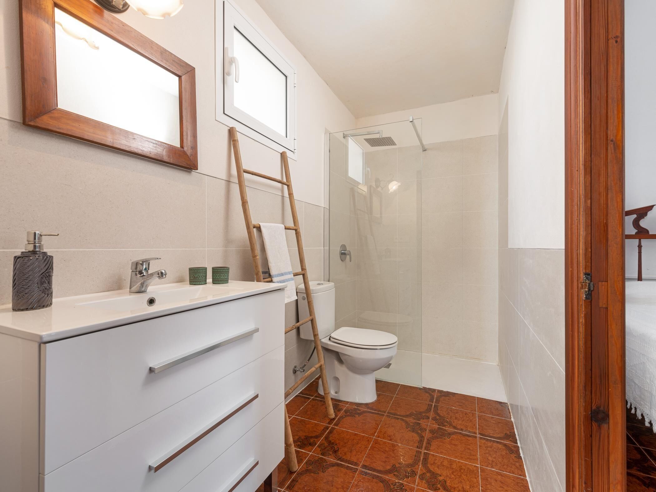 A bathroom with a white vanity, a toilet, a shower, and a wooden ladder.