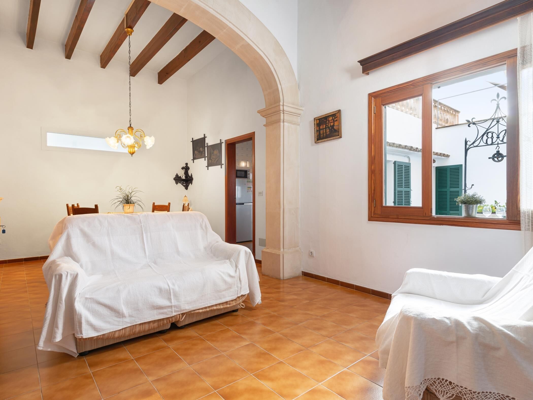 Um quarto aconchegante com sofá estofado, mesa de jantar com cadeiras, um candelabro e uma janela grande com persianas.