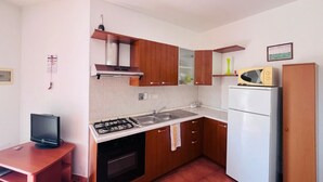 A compact kitchen with wooden cabinets, a gas stove, a sink, and a white refrigerator. - Casa Solana al Cavo meters from the sea (Cavo)