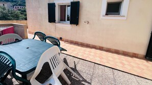 A patio with a table and chairs, a small window, and a view of a hill. - Casa Solana al Cavo meters from the sea (Cavo)