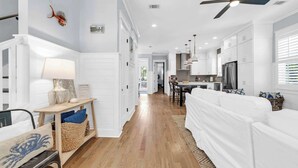 Una cocina moderna con armarios blancos, un comedor con mesa y sillas, y un pasillo que conduce a una sala de estar con sofá blanco.
