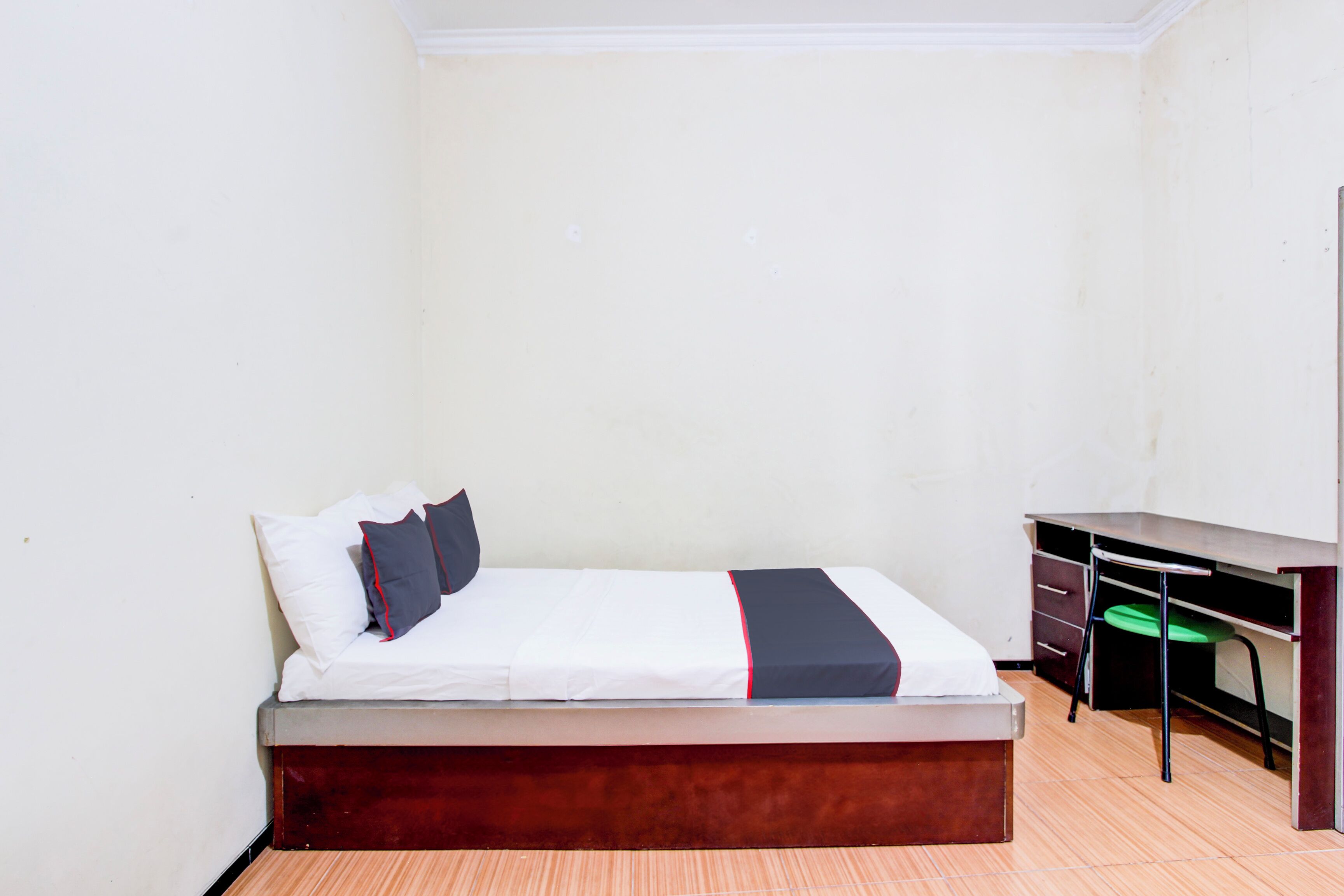 A single bed with a wooden frame, a desk with a chair, and a green seat cushion.